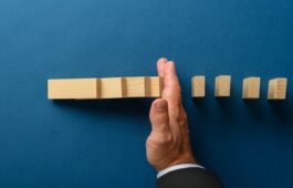 Top view of businessman hand interfering to stop collapsing dominos. Over blue background.