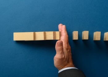 Top view of businessman hand interfering to stop collapsing dominos. Over blue background.