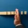 Top view of businessman hand interfering to stop collapsing dominos. Over blue background.